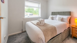 A bedroom with a bed, a window with blinds, a radiator, a wooden nightstand, and a lamp.