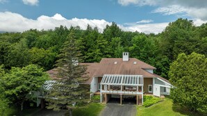 A modern house with a large deck, surrounded by dense forest. - Mountain condo by Sugarbush w/ fireplace (Warren)