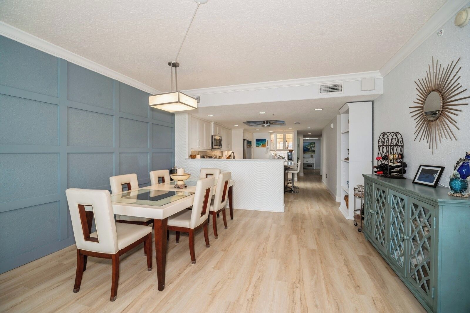 Una cocina moderna con armarios blancos, una isla central y una zona de comedor con mesa de vidrio y sillas.