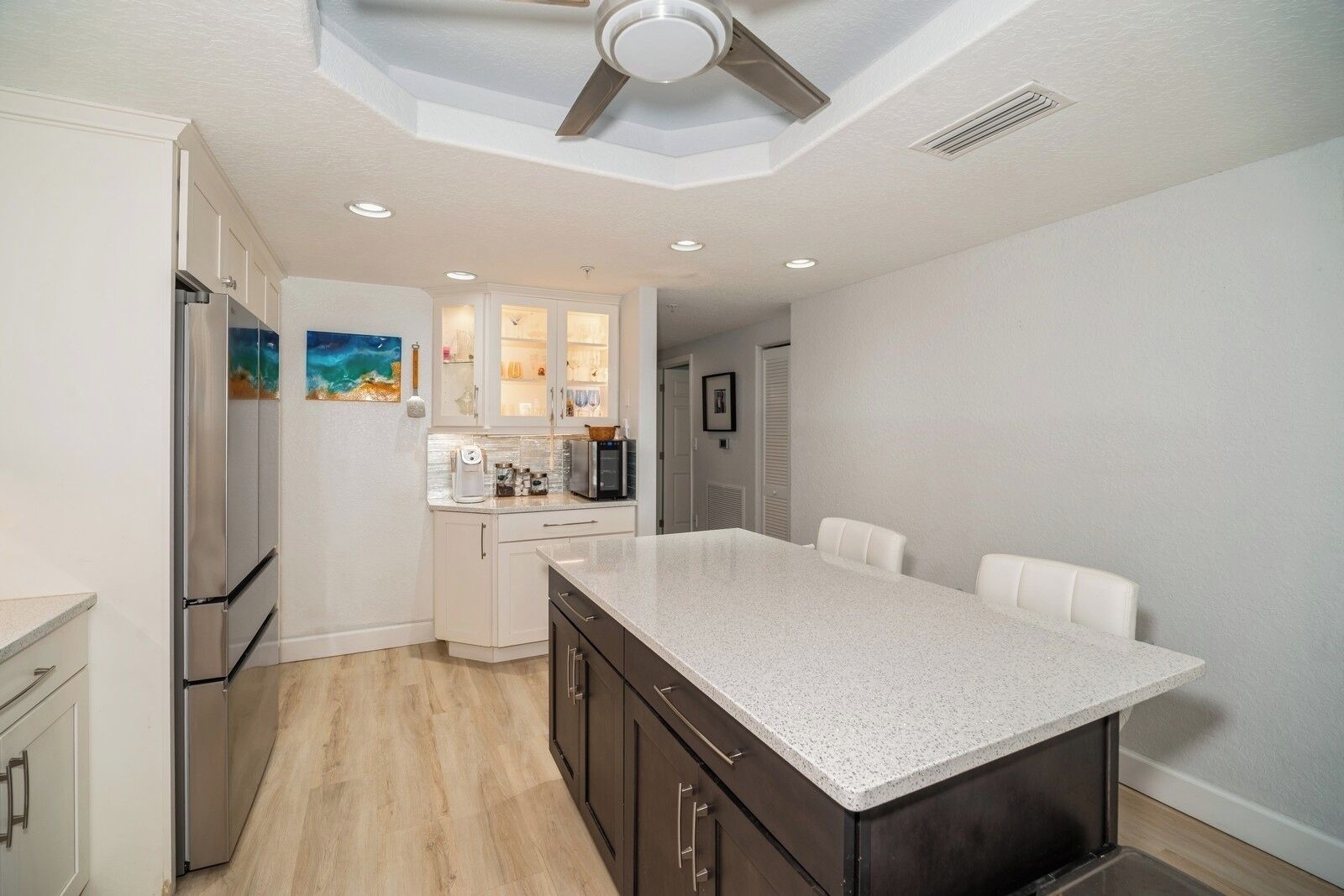 A modern kitchen with a central island, white cabinetry, and a ceiling fan.