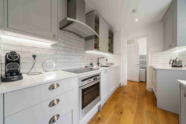 A modern kitchen with white cabinetry, a built-in oven, and a coffee machine.