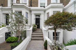 A traditional building with a central staircase leading to a door, surrounded by white walls and greenery.