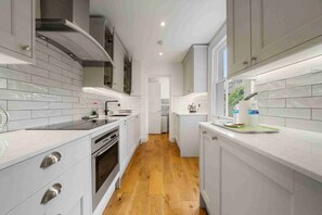 A modern kitchen with white cabinetry, a stainless steel range, and a wooden floor.