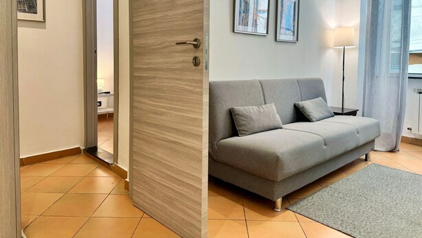A modern living room with a grey sofa, a small rug, and two framed pictures on the wall. - [Aquarium] Porto Antico Vanilla Apartment (Genova)