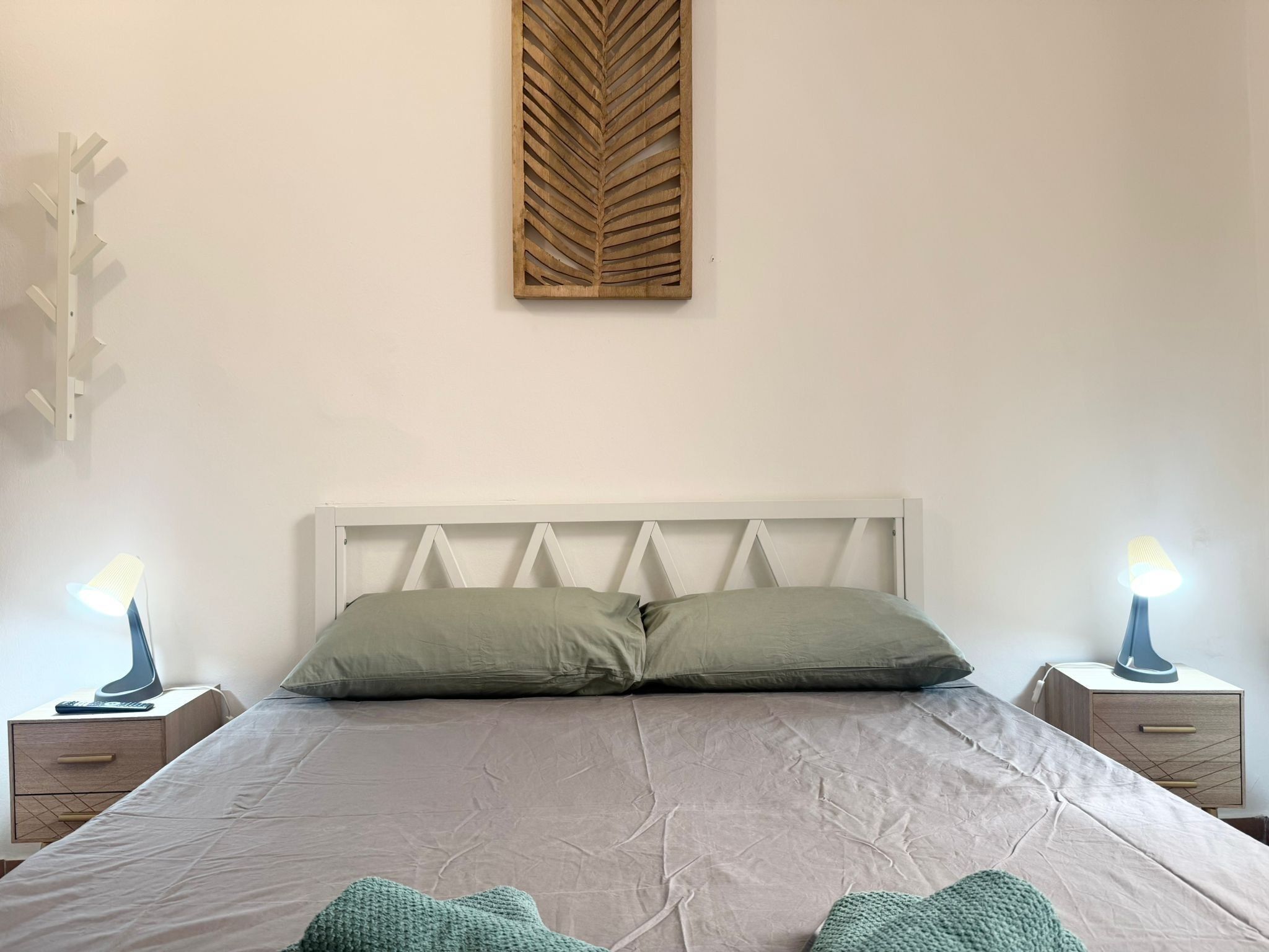Ein Bett mit weißem Kopfteil, zwei Nachttische mit Lampen und eine an der Wand befestigte Holz-Blattdeko.
