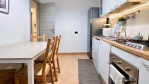 A compact kitchen with a wooden dining table and chairs, a microwave, a stove, and a sink. - [Aquarium] Porto Antico Vanilla Apartment (Genova)
