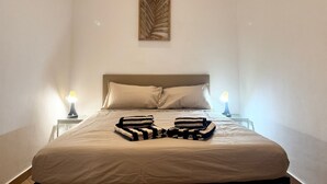A neatly made bed with a beige comforter and pillows, two bedside lamps, and a decorative wooden panel above the bed. - [Aquarium] Porto Antico Vanilla Apartment (Genova)