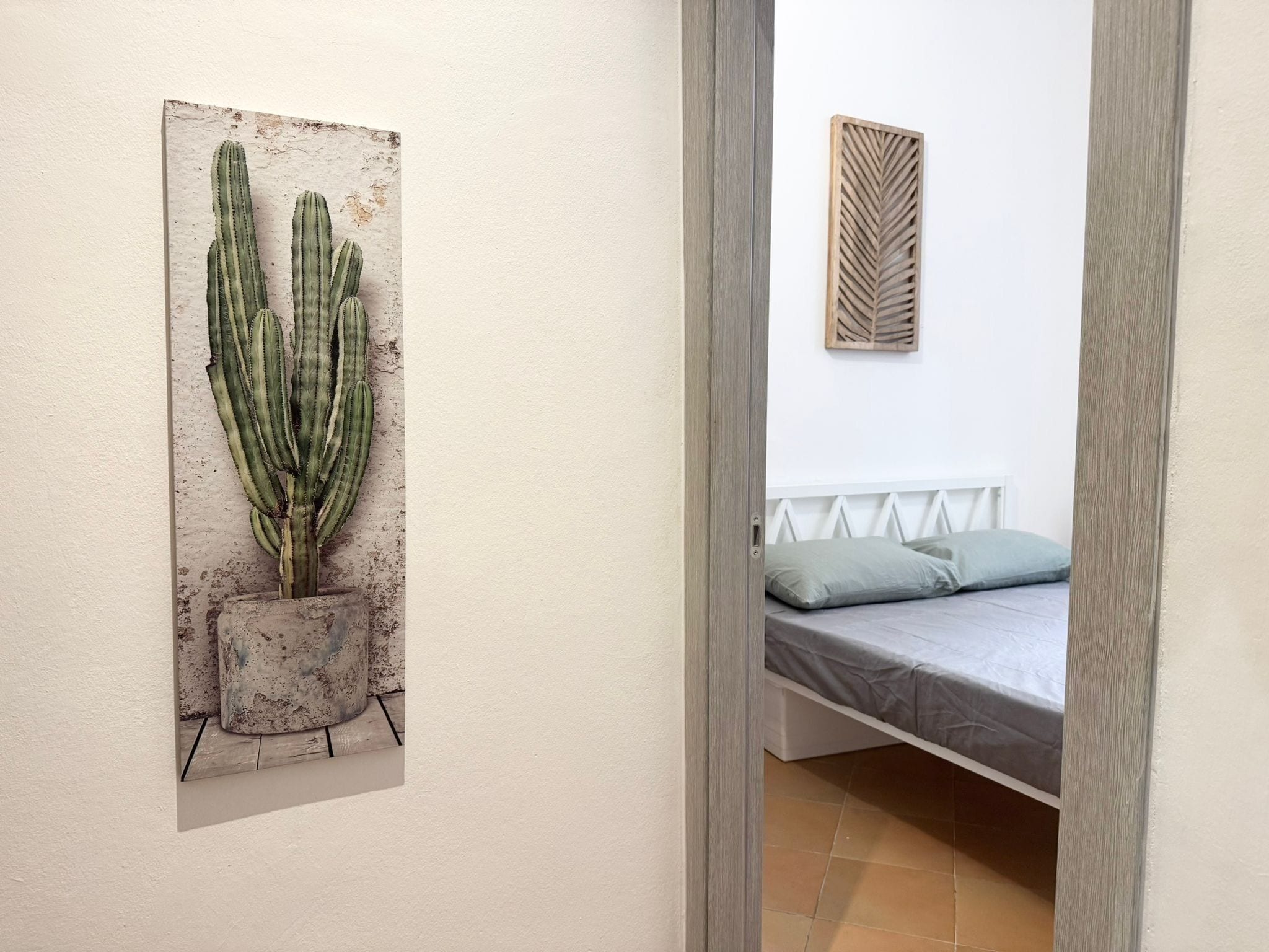 Une chambre à coucher comprenant un lit, une œuvre d’art représentant un cactus accrochée au mur, et un panneau décoratif en bois.