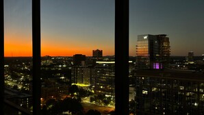 Une vue d’une ville au crépuscule, avec des bâtiments illuminés et un bâtiment en forme de W qui se distingue particulièrement.