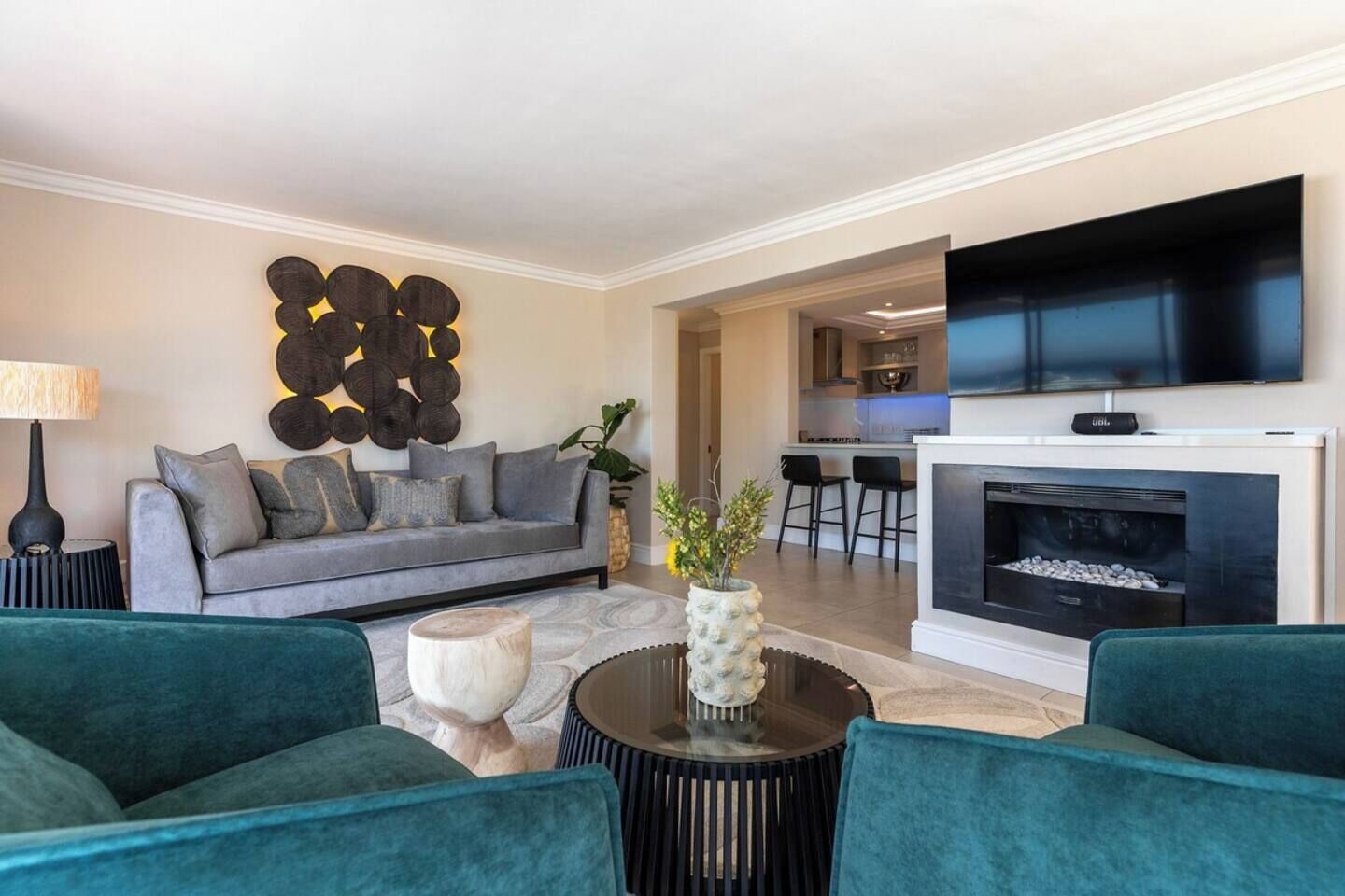 Un salon moderne avec un canapé gris, des fauteuils turquoise, une table basse ronde et une cheminée.