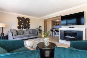 A modern living room with a grey sofa, teal armchairs, a round coffee table, and a fireplace. - Your CT experience starts here (Cape Town)