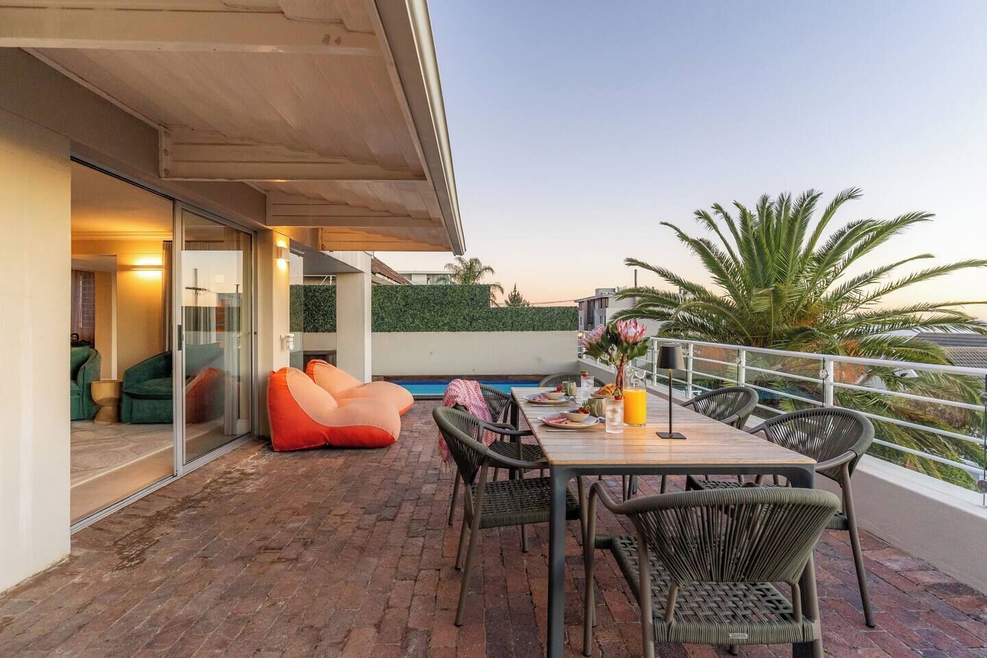 An outdoor patio with a dining table, chairs, a pool, and a glass-enclosed room.