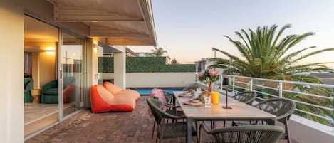 Une terrasse extérieure avec une table à manger, des chaises, une piscine et une pièce fermée par des parois de verre.