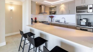 A modern kitchen with a central island, bar stools, stainless steel appliances, and a built-in oven.
