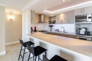 A modern kitchen with a central island, bar stools, stainless steel appliances, and a built-in oven. - Your CT experience starts here (Cape Town)