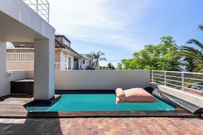 A rooftop swimming pool with a clear blue water surface, a lounge area with a cushioned seating arrangement, and a view of neighboring buildings and greenery. - Your CT experience starts here (Cape Town)