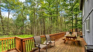 A wooden deck with outdoor furniture, surrounded by a forest.