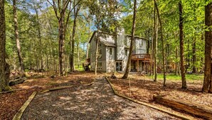 A rustic cabin surrounded by a forest with a gravel path leading to it.