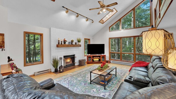 A spacious living room with a fireplace, large windows, a ceiling fan, and a leather sofa.