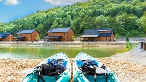 A lakeside cabin area with three wooden cabins and kayaks on a pebble beach. - Close to Thunder Ridge, Luxury Cabin, Pools (Hollister)