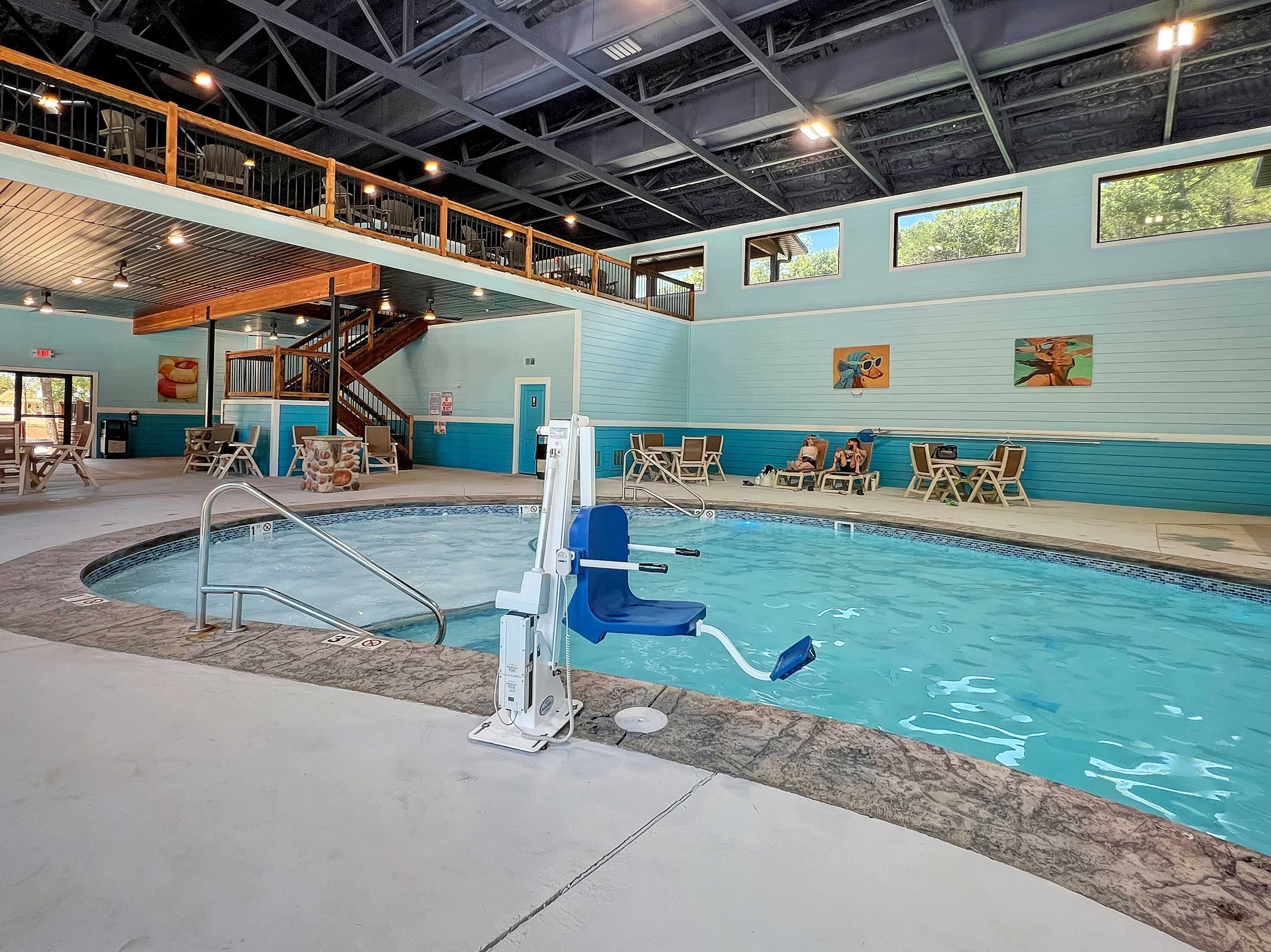 An indoor swimming pool with a lifeguard stand, lounge chairs, and a mezzanine level with seating.