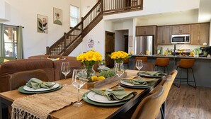 A dining area with a wooden table set for six, a staircase, and a kitchen in the background. - Close to Thunder Ridge, Luxury Cabin, Pools (Hollister)