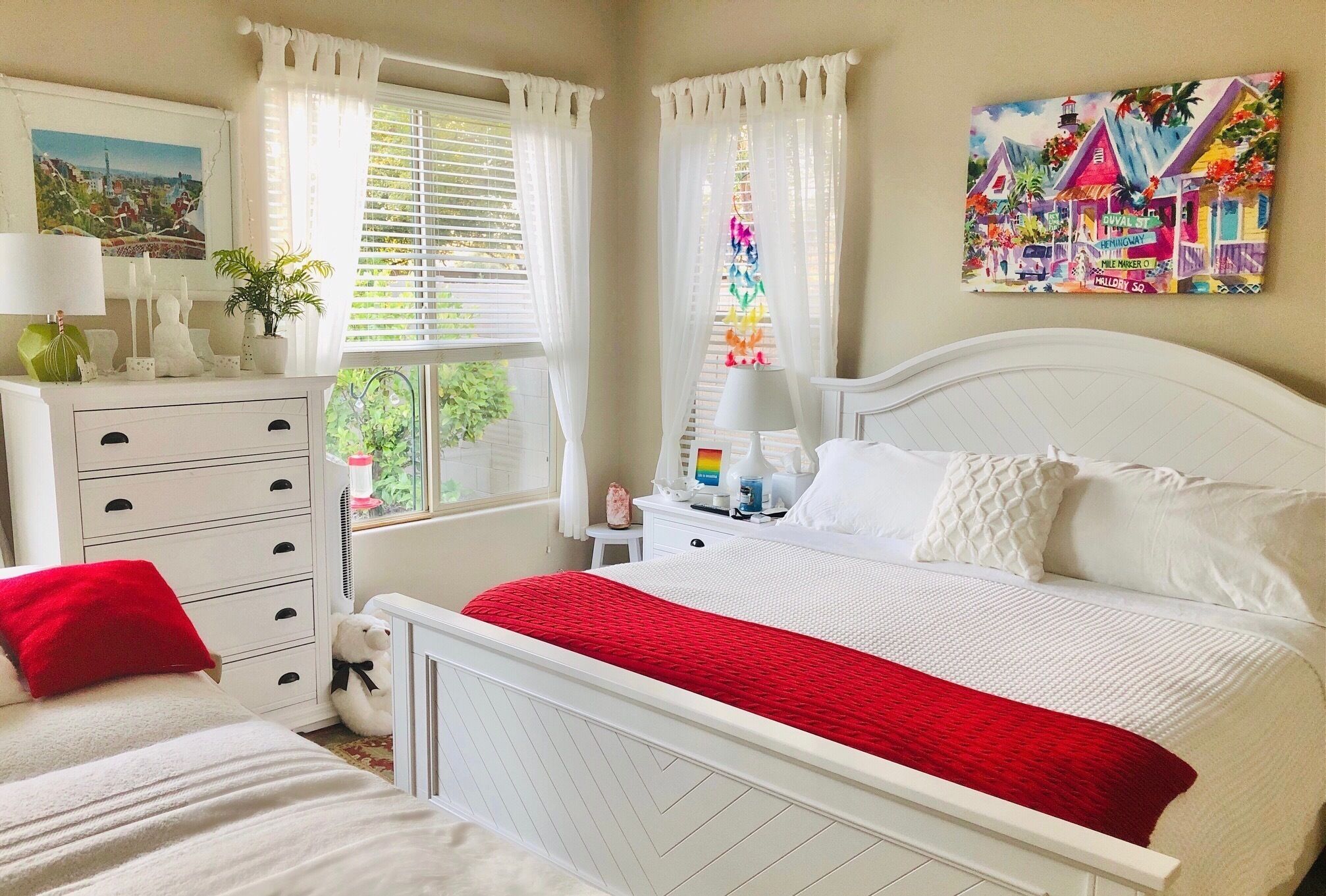 A bedroom with a bed, a dresser, a nightstand, and a window with curtains.