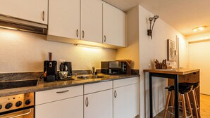 Cocina moderna con armarios blancos, horno empotrado, cafetera y microondas. Hay taburetes en una mesa pequeña.