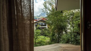 Una terraza de madera con vistas a un edificio rodeado de vegetación y montañas.