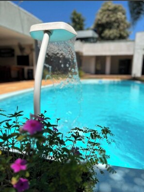 A swimming pool with a water feature, surrounded by greenery and modern architecture.