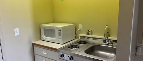 A compact kitchenette with a microwave, stove, and sink.