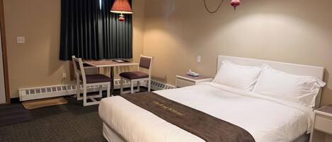 A hotel room with a bed, a desk, two chairs, a table, a lamp, and a heater.