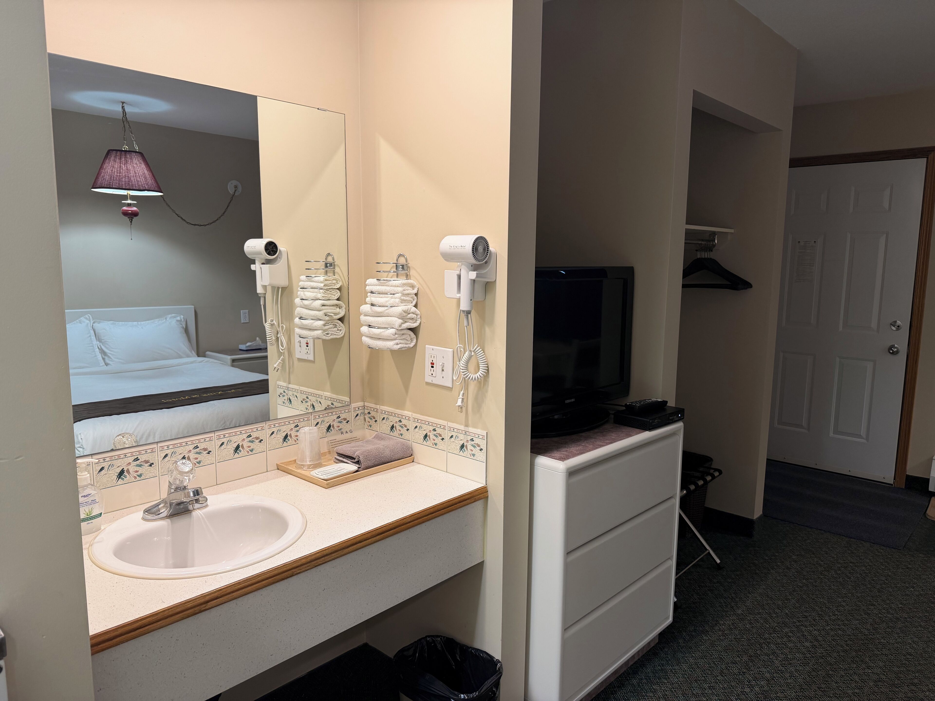 Une salle de bain d’hôtel équipée d’un lavabo, d’un miroir, d’un porte-serviettes, d’un sèche-cheveux et d’un téléviseur.