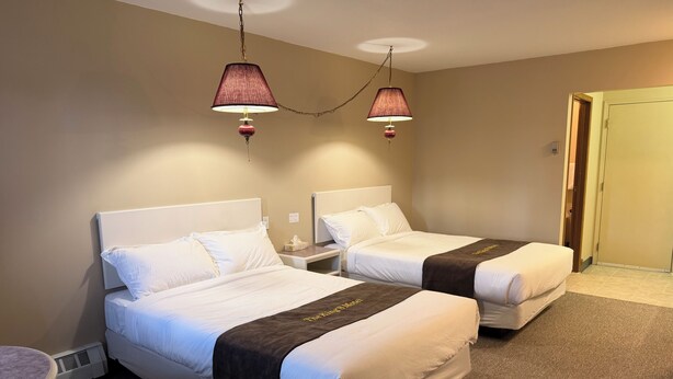 Ein Hotelzimmer mit zwei Betten, einem Nachttisch, einer Lampe und einer Tür.