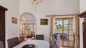 Ein Essbereich mit Tisch, Stühlen und einer Chandelier. Eine Tür führt zu einem Balkon mit Gartenmöbeln.