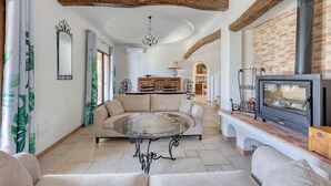A living room with a round glass table, a sofa, a fireplace, and a wooden ceiling beam.