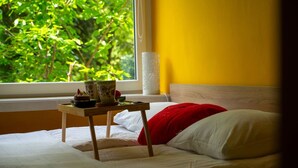 A bed with white bedding, a red pillow, and a small wooden table with a tray of items.