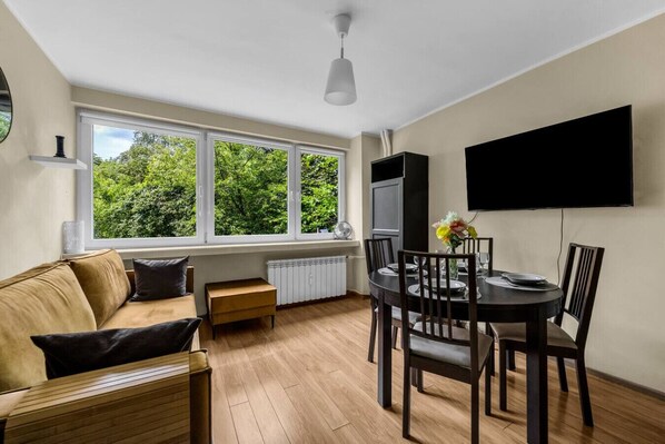 Una sala de estar moderna con un sofá, una mesa de comedor para cuatro personas y un ventanal con vista a follaje.