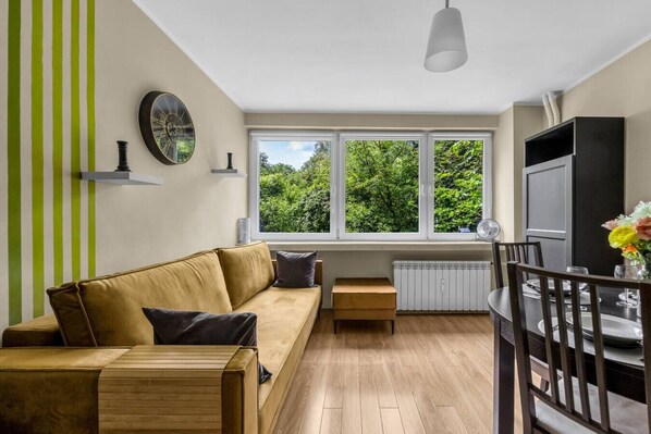 Un salon moderne comprenant un canapé, une table à manger avec des chaises, un téléviseur et une grande fenêtre donnant sur un paysage verdoyant.