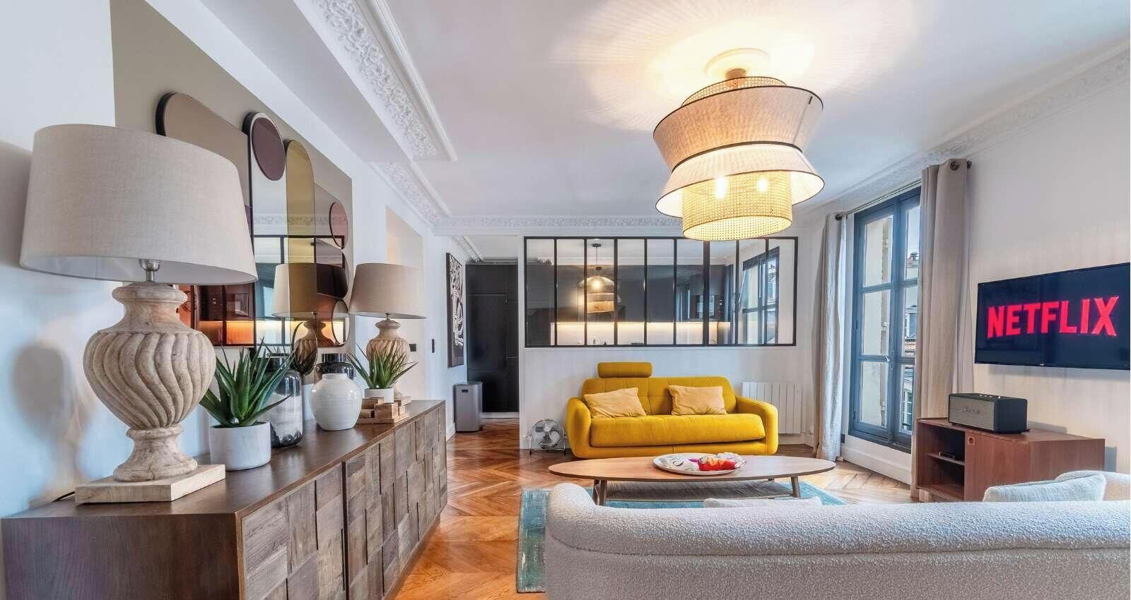 Una sala de estar moderna con un sofá amarillo, una mesa de centro y un televisor mostrando 'NETFLIX'.