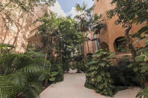 A courtyard with a pathway surrounded by lush greenery and architectural arches. - Serene 2BR Apartment with Private Pool, Kokoon Pueblo II (Tulum)