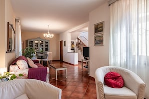 Ein Wohnzimmer mit Sofa, Sessel, Esstisch, einer Kronleuchter und einer Treppe zu einer weiteren Ebene.