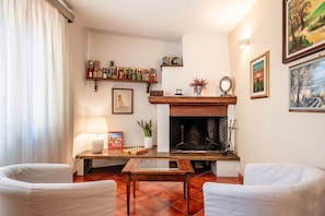 Un salon avec une cheminée, une table basse, deux fauteuils, une lampe, une bibliothèque et des tableaux encadrés accrochés aux murs.