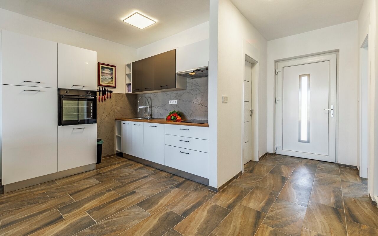 A modern kitchen with white cabinets, a built-in oven, and a marble backsplash.