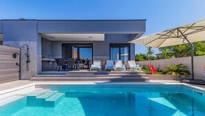 A modern outdoor pool area with a pool, lounge chairs, and a dining area with a table and chairs. - Istriensonne 0785 - Newly built semi-detached house Double1 with private pool (Loborika)