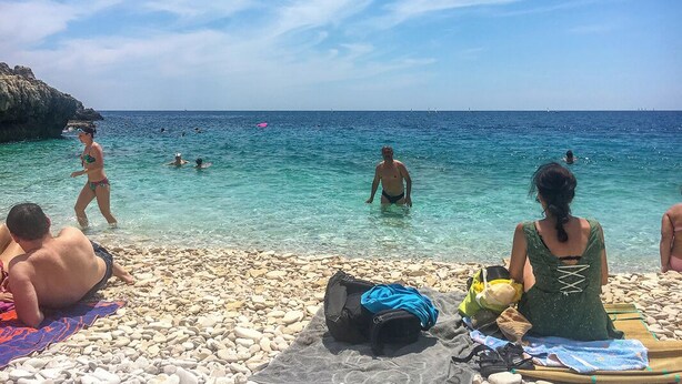 A pebbled beach with people swimming and sunbathing, clear blue water, and a rocky cliff in the background. - Istriensonne 0785 - Newly built semi-detached house Double1 with private pool (Loborika)