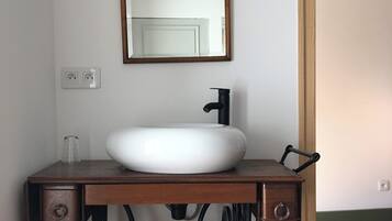 Un baño con un lavamanos sobre la base antigua de una Singer, un lavabo blanco y un espejo con marco de madera.
