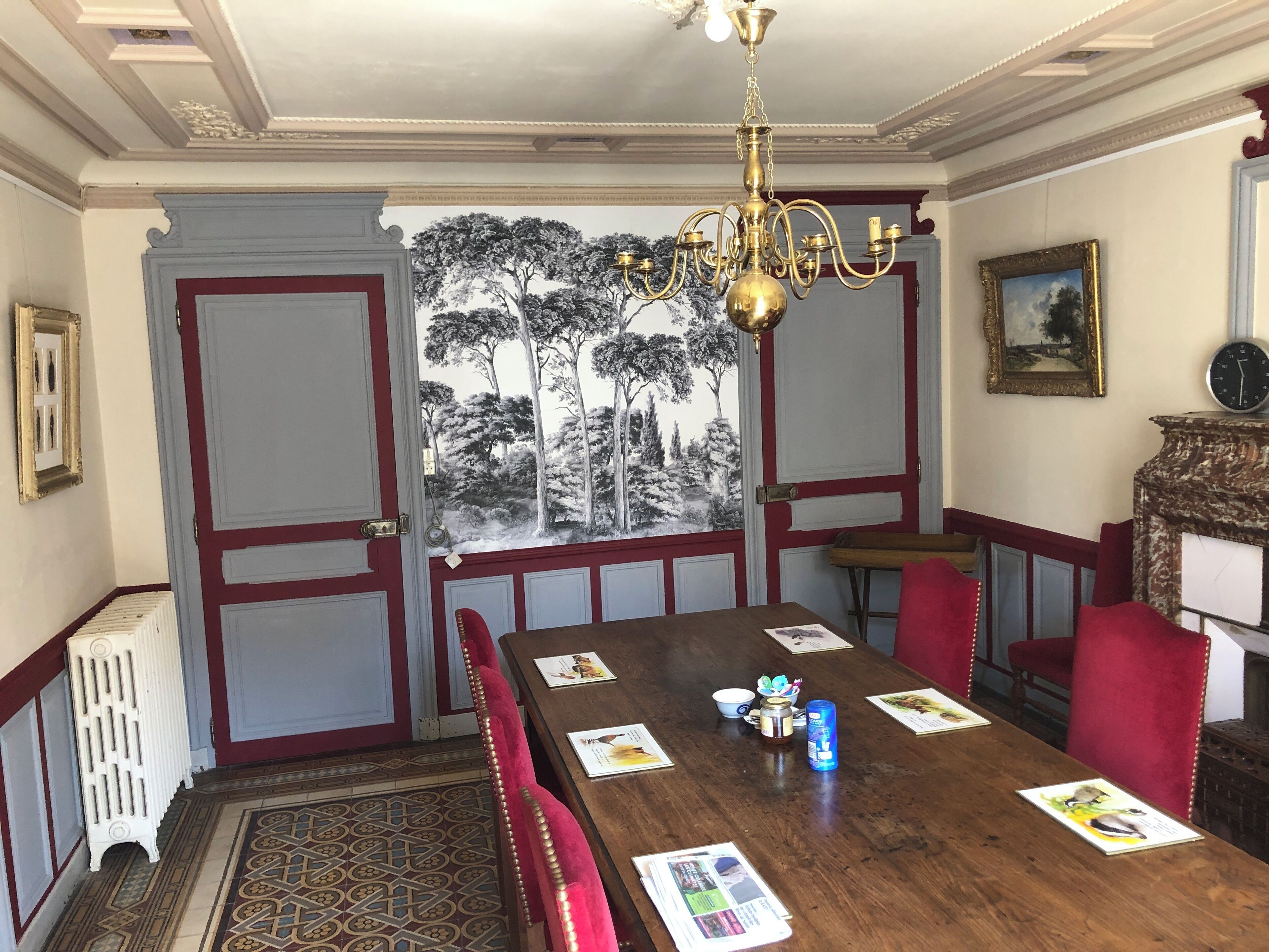 Un coin repas avec une table en bois, des chaises à revêtement rouge, un lustre et une horloge murale.