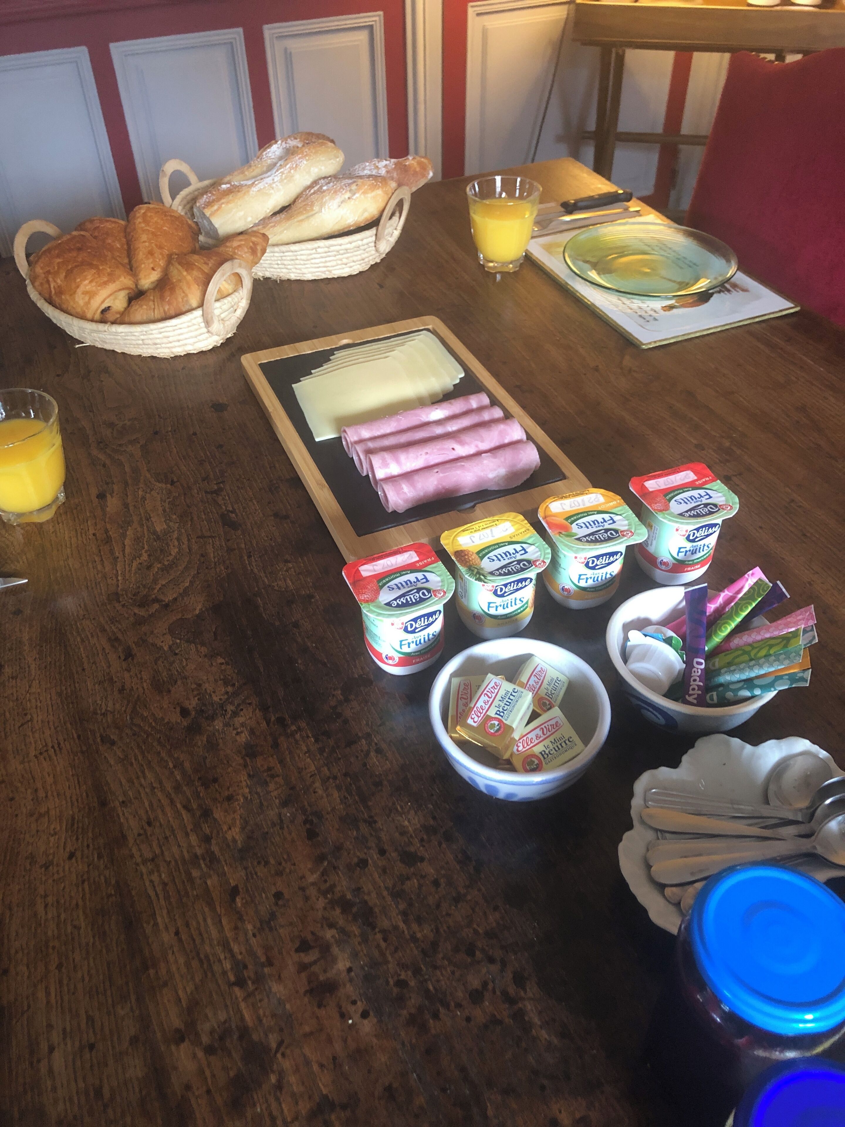Una mesa de desayuno con cruasanes, queso, jamón, yogur de frutas y jugo.