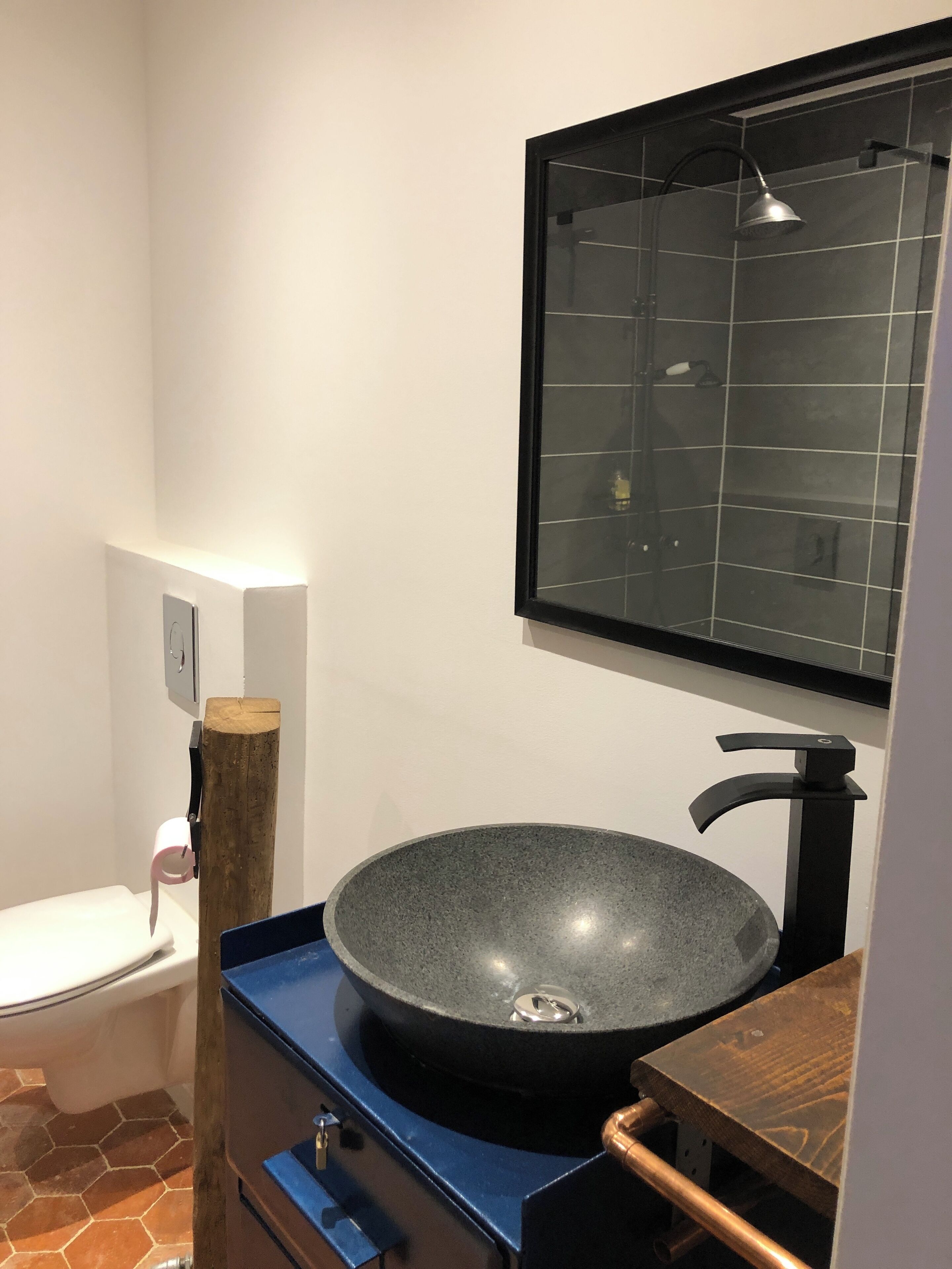 Een badkamer met een groot, rond, donker wastafel, een moderne kraan en een spiegel erboven.